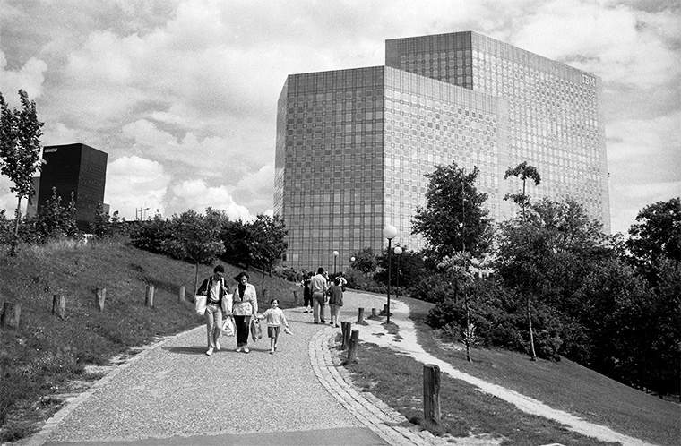 En arrière-plan, on peut apercevoir un bâtiment monstrueux, avec le couple rentrant avec ses achats et sa petite fille, Paris-la-Défense, juillet 1987.