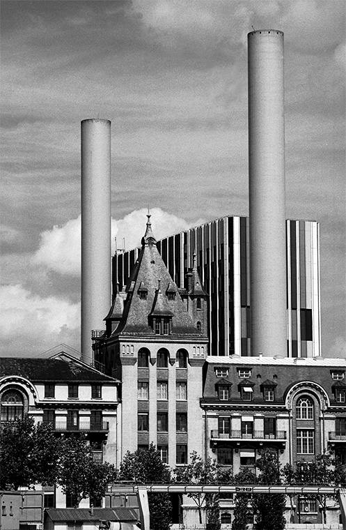 Des cheminées imposantes, au premier plan un édifice ancien et à l'arrière des bureaux modernes.