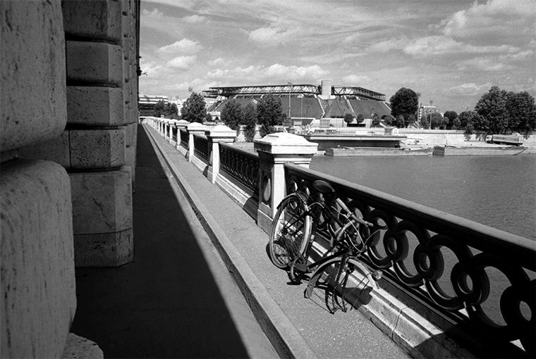 Sur le pont, on peut voir un vélo dont la roue a été enlevée. À l'arrière-plan, on peut voir la salle de Bercy, Paris Bercy, juillet 1987.
