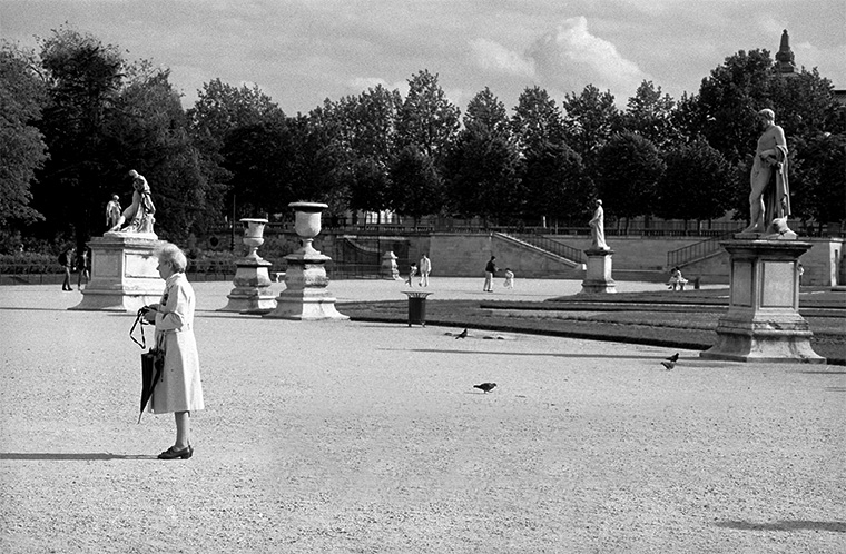 Sous un ciel d’été incertain, une dame attend, parapluie à la main, aux Tuileries, Paris, juin 1987.